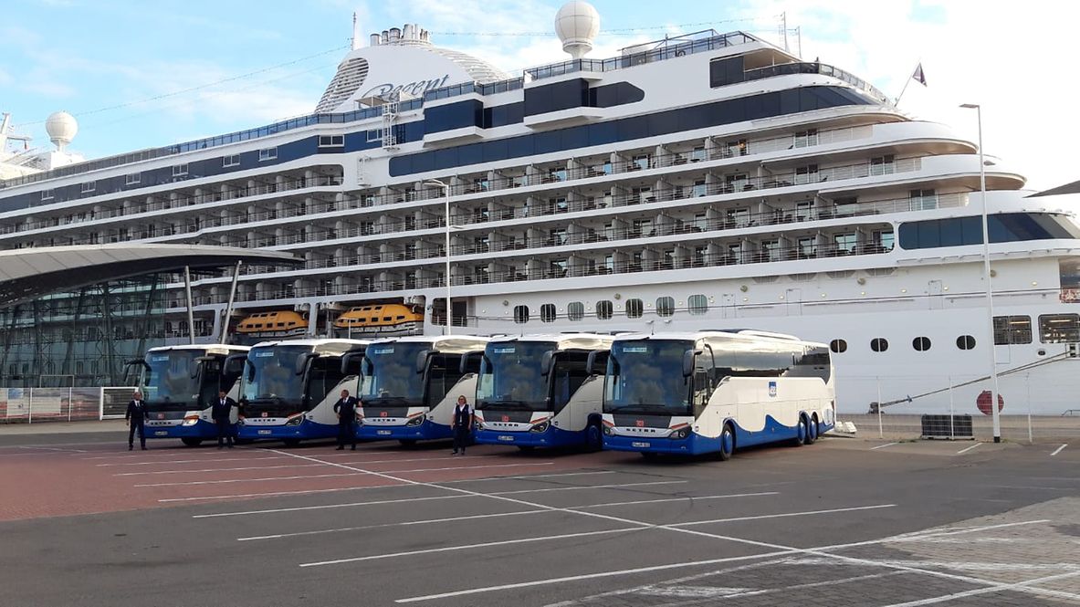 UBB Busse stehen in einer Reihe vor einem Kreuzfahrtschiff
