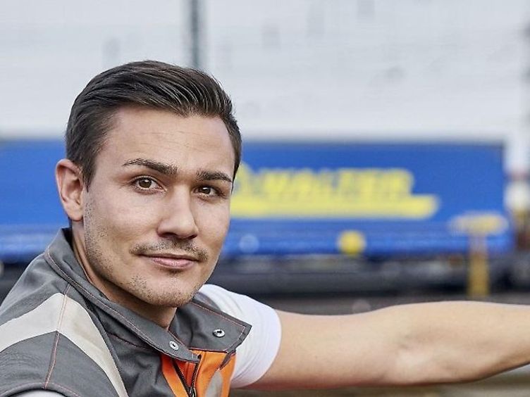 Junger Mann schaut seitlich in die Kamera. Er hat Arbeitskleidung an