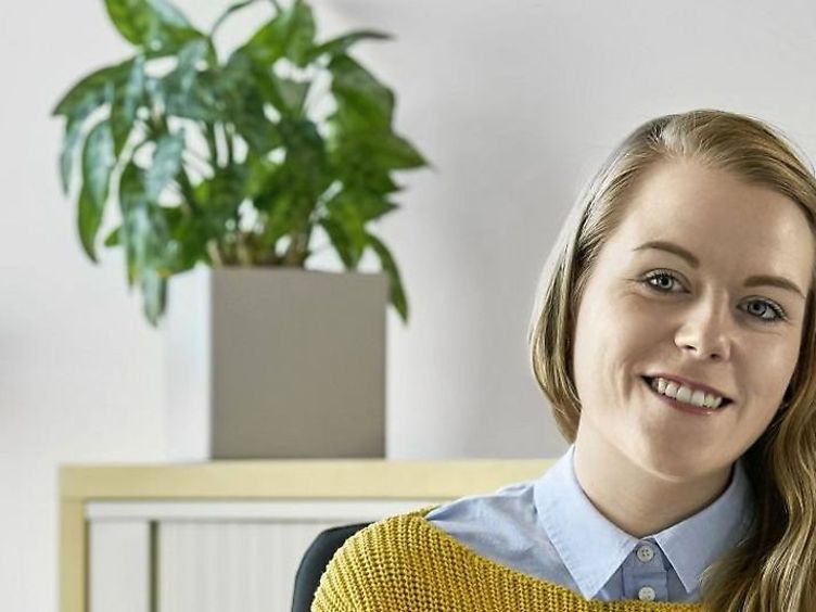 Frau schaut in die Kamera, im Hintergrund steht eine Zimmerpflanze