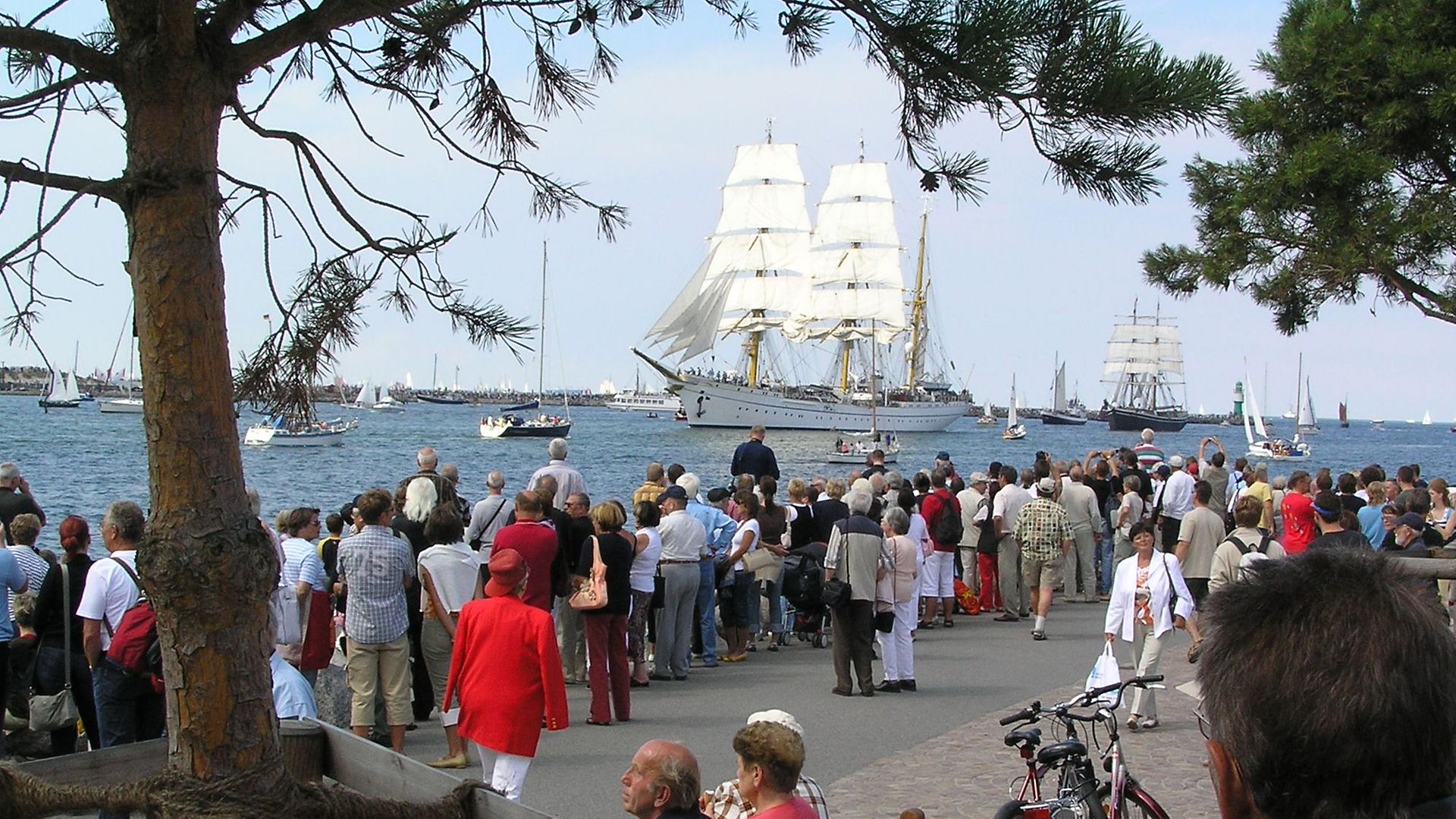 Eine Gruppe von Menschen schauen sich Segelschiffe auf dem Wasser an